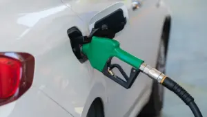 Degvielas uzpildes pistole ievietota baltas automašīnas bākā degvielas uzpildes stacijā.