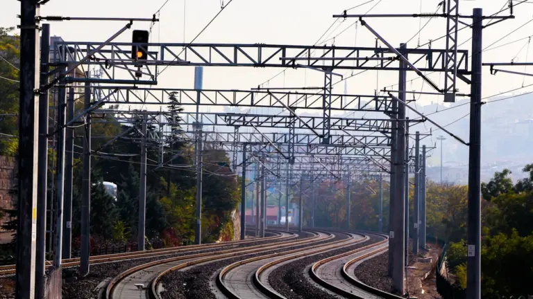 Dzelzceļa sliedes ar elektrifikācijas līniju, kas simbolizē Rail Baltica modernizāciju Latvijā.
