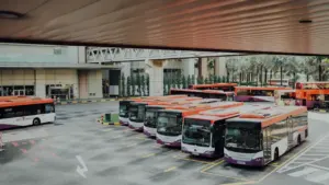 Autobusu parks ar vairākiem baltiem un oranžiem autobusiem gaida savu izbraukšanas laiku