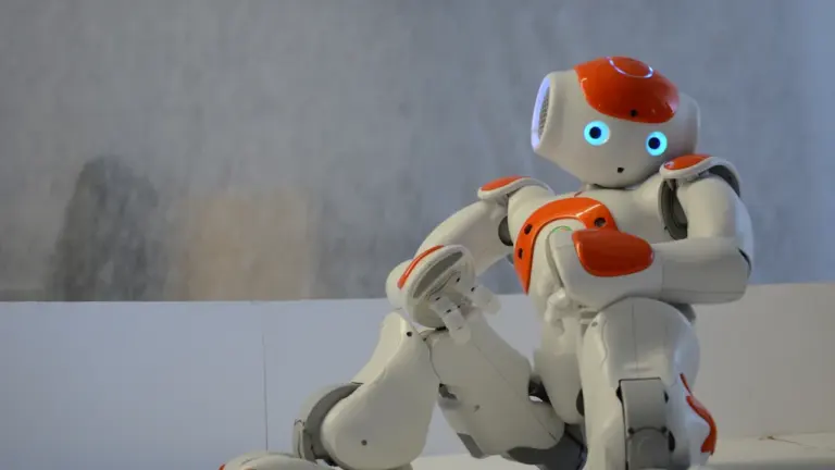 Mazs, balts un oranžs robots sēž un vēro apkārtni Slampes pasākumā