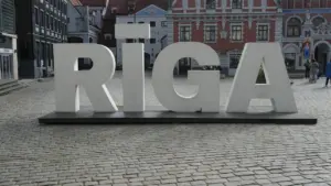Liels, balts uzraksts RĪGA uz bruģētas ielas vēsturiskajā Rīgas centrā.