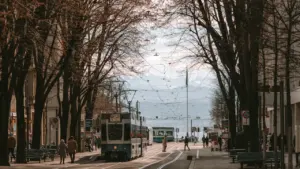 Cilvēki staigā pa Bahnhofstrasse ielu Cīrihē, kurā redzams tramvajs un koki.